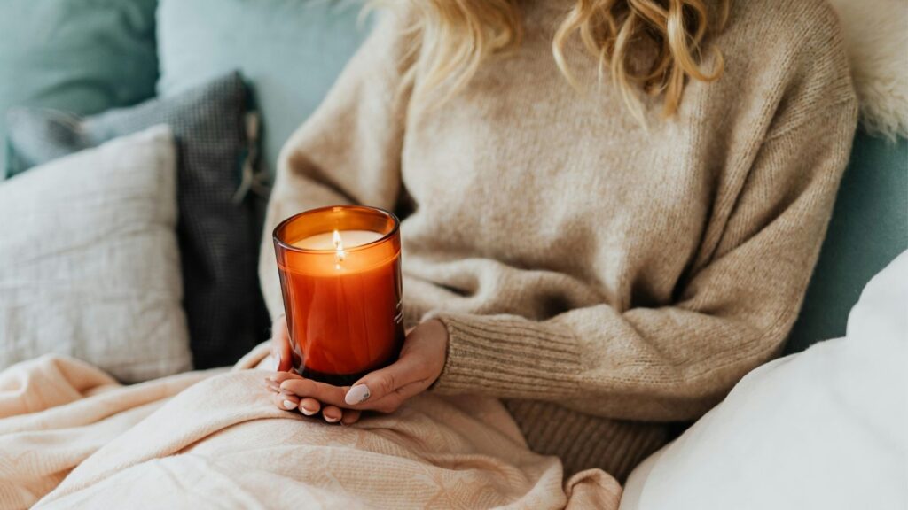 Frau sitzt entspannt auf der Couch mit Kerze in der Hand, ganzheitlicher Umgang mit Blasengesundheit