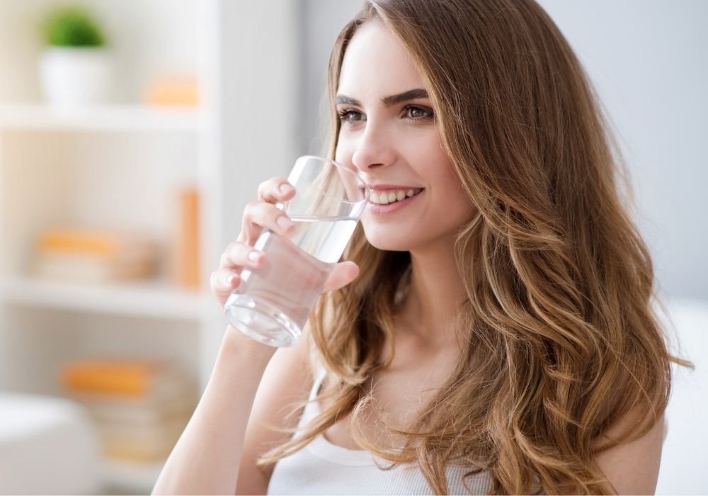 Frau lächelt und trinkt Wasser aus einem Trinkglas.