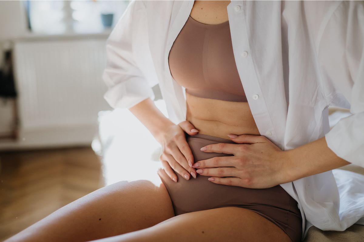 Frau hält sich den Bauch – typische Symptome wie Blähbauch oder Verdauungsprobleme können auf eine gestörte Darmflora hinweisen.