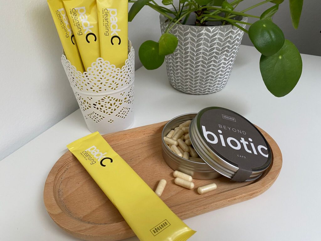 ringana pack cleansing sachet und caps biotic auf Holztablett mit Pflanze im Hintergrund